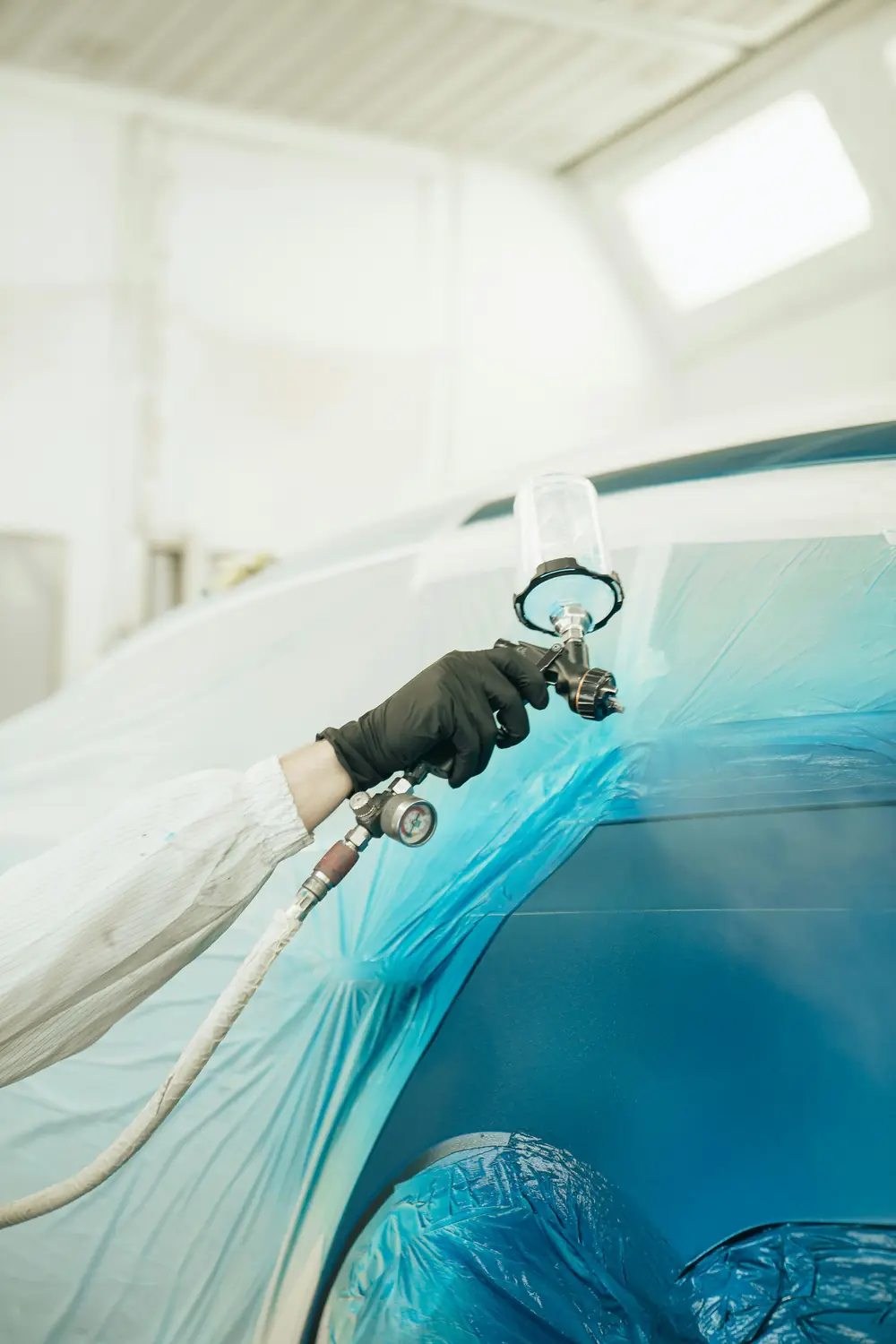 A technician spray-painting a car body in a refinish booth